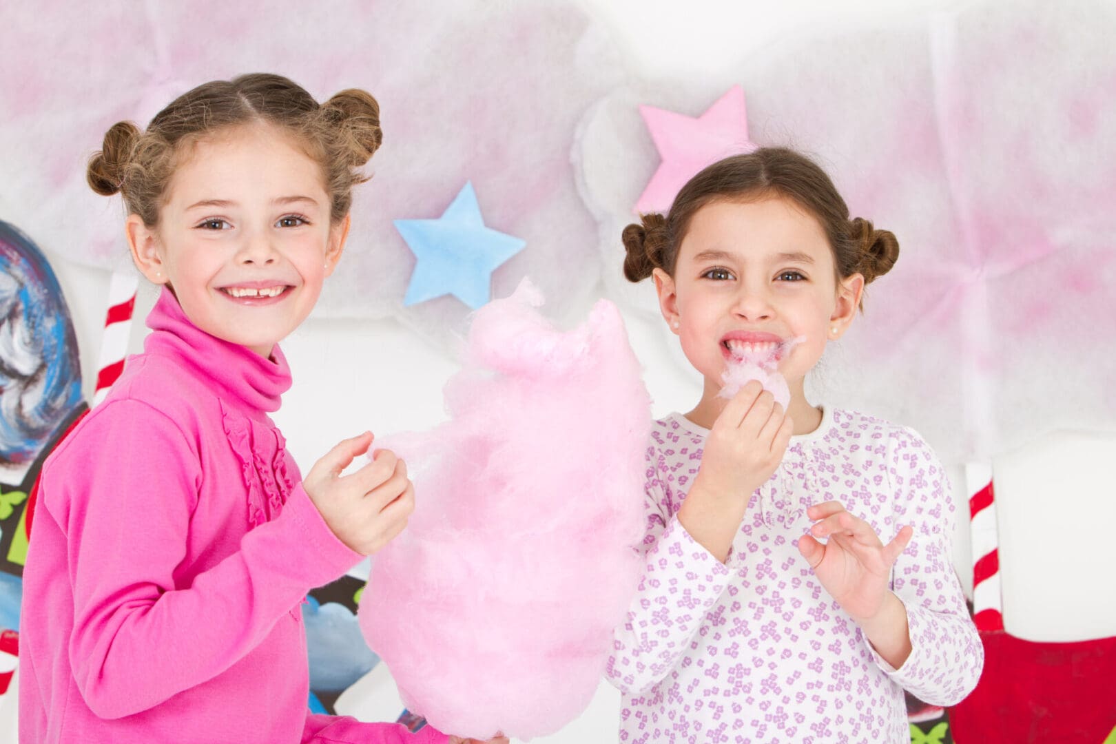 Two girls are eating cotton candy in a room.